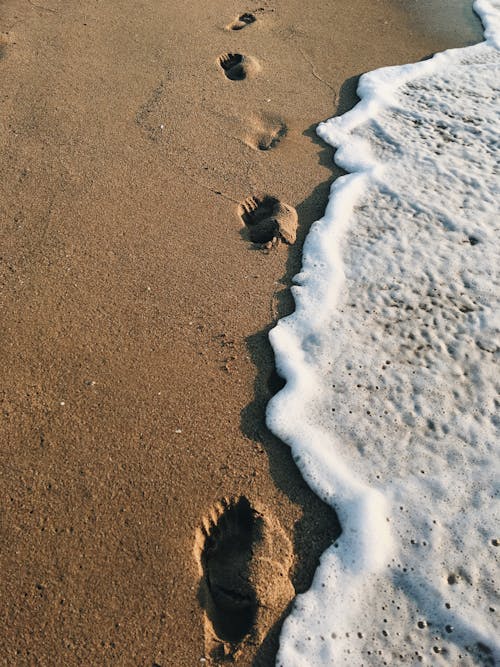 Free From above footprints located on sandy beach near wave of sea water with white foam on resort Stock Photo