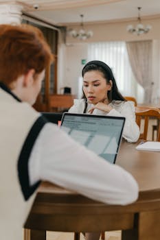 Professional meeting with two adults using laptops at a wooden table indoors.