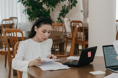 A Woman in White Dress Sitting on Wooden Chair while Studying 