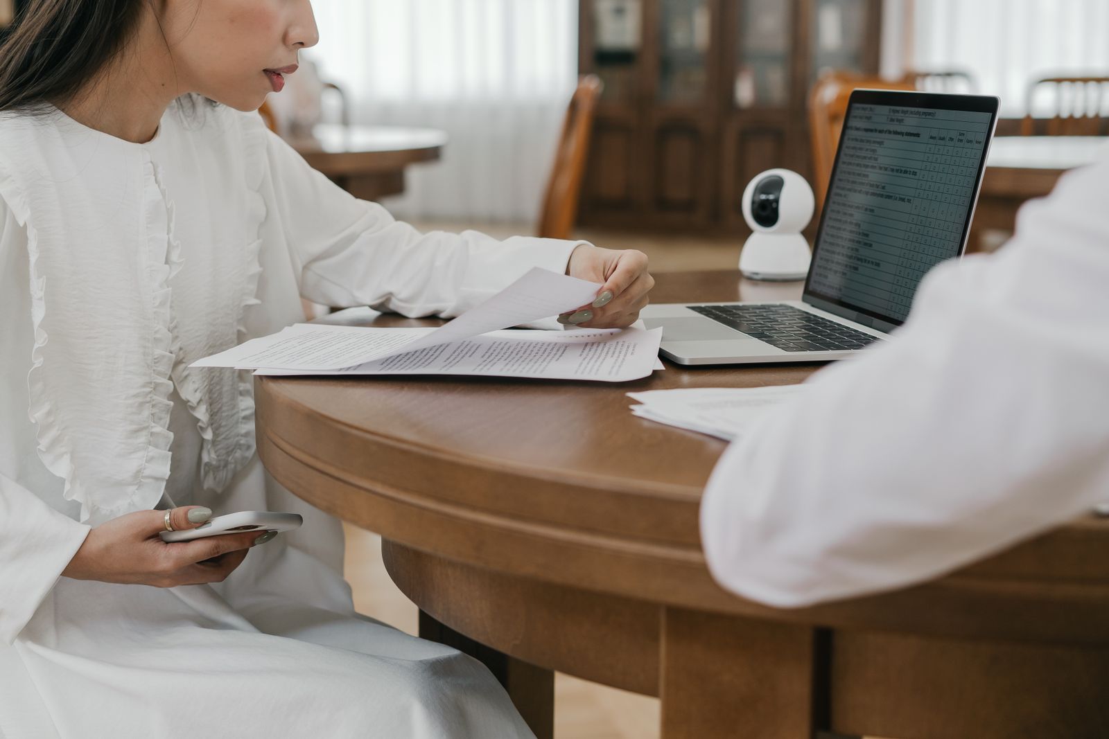 Mujer revisando documentos y su teléfono junto a una computadora durante una solicitud online