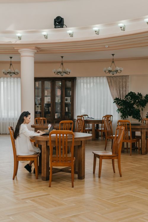 Free A woman studies in a spacious library with wooden furniture, offering a cozy academic ambiance. Stock Photo
