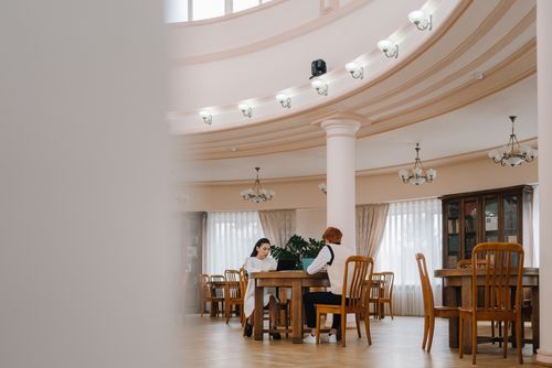 Free Two students studying at wooden tables in stately library with laptops and books. Stock Photo