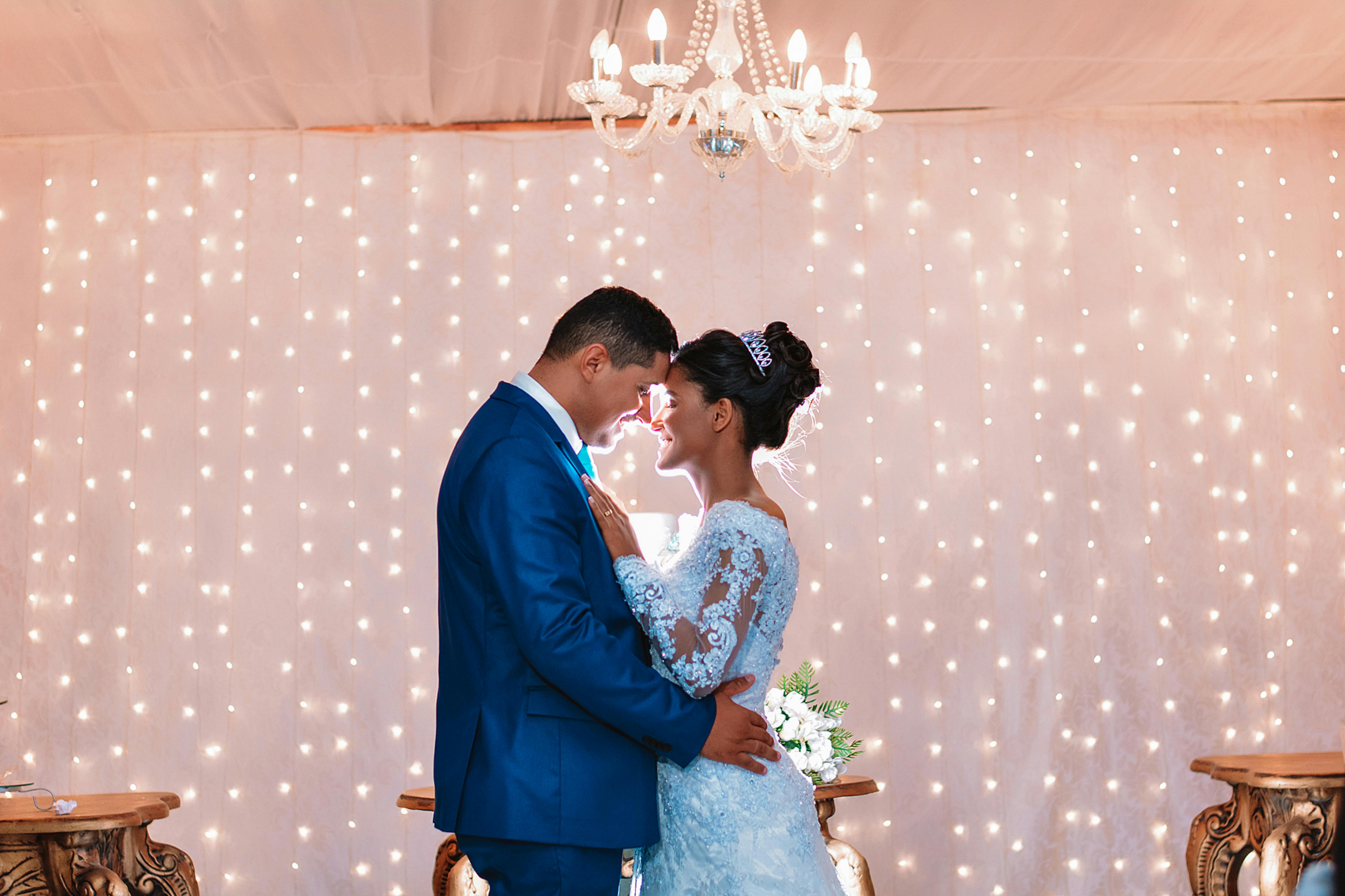 An intimate embrace of a couple in wedding attire under elegant chandelier lighting.