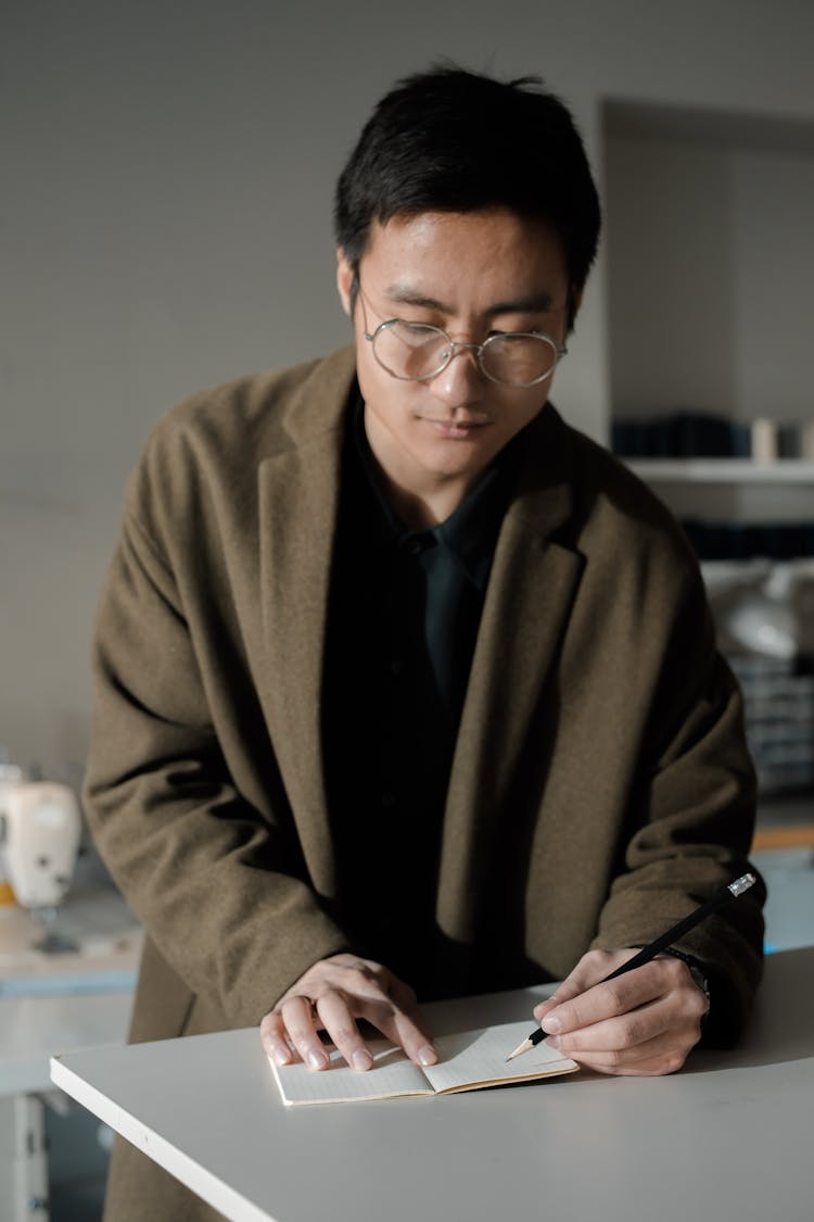 Man Wearing Coat Writing On A Notebook