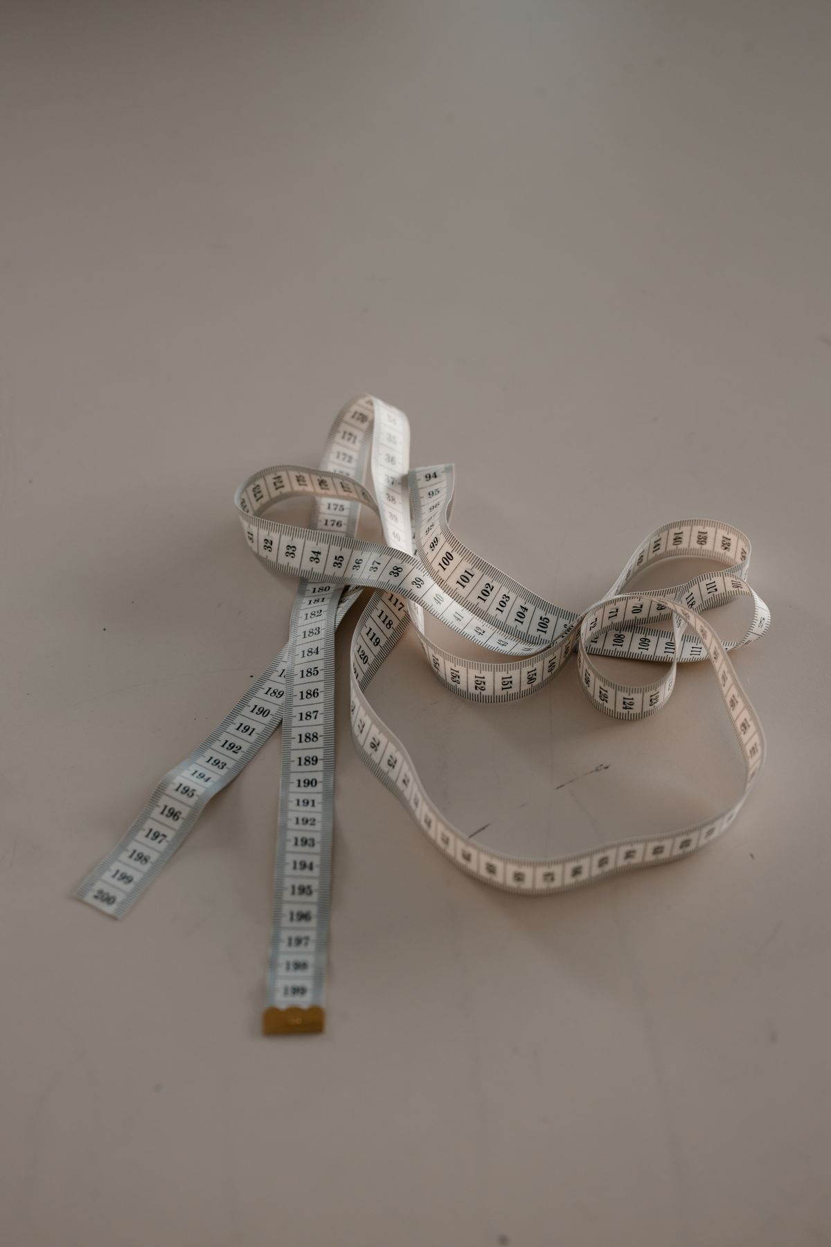 A white cloth measuring tape coiled on a plain surface