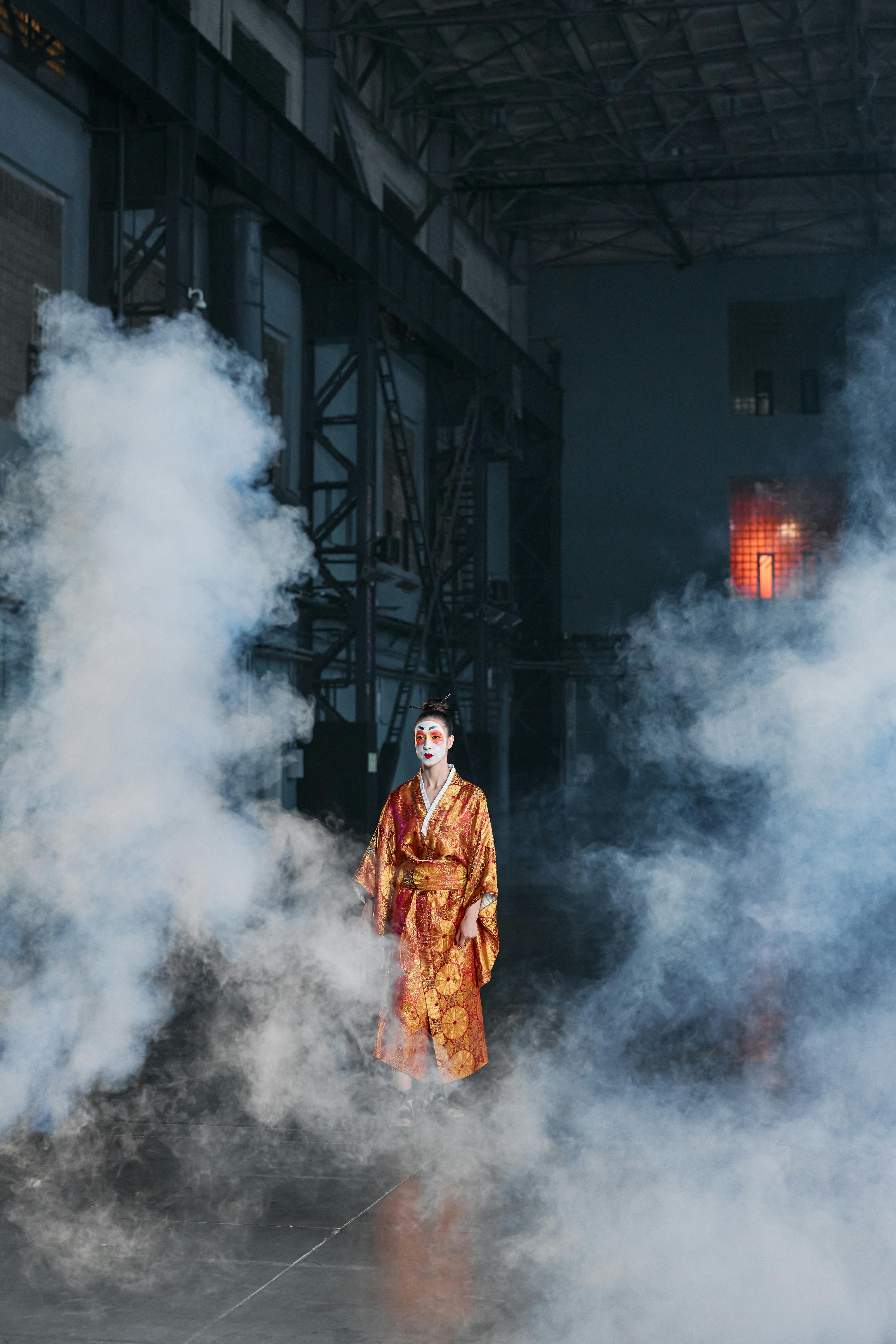 Free Geisha wearing a traditional kimono amidst a smoky, atmospheric industrial setting. Stock Photo