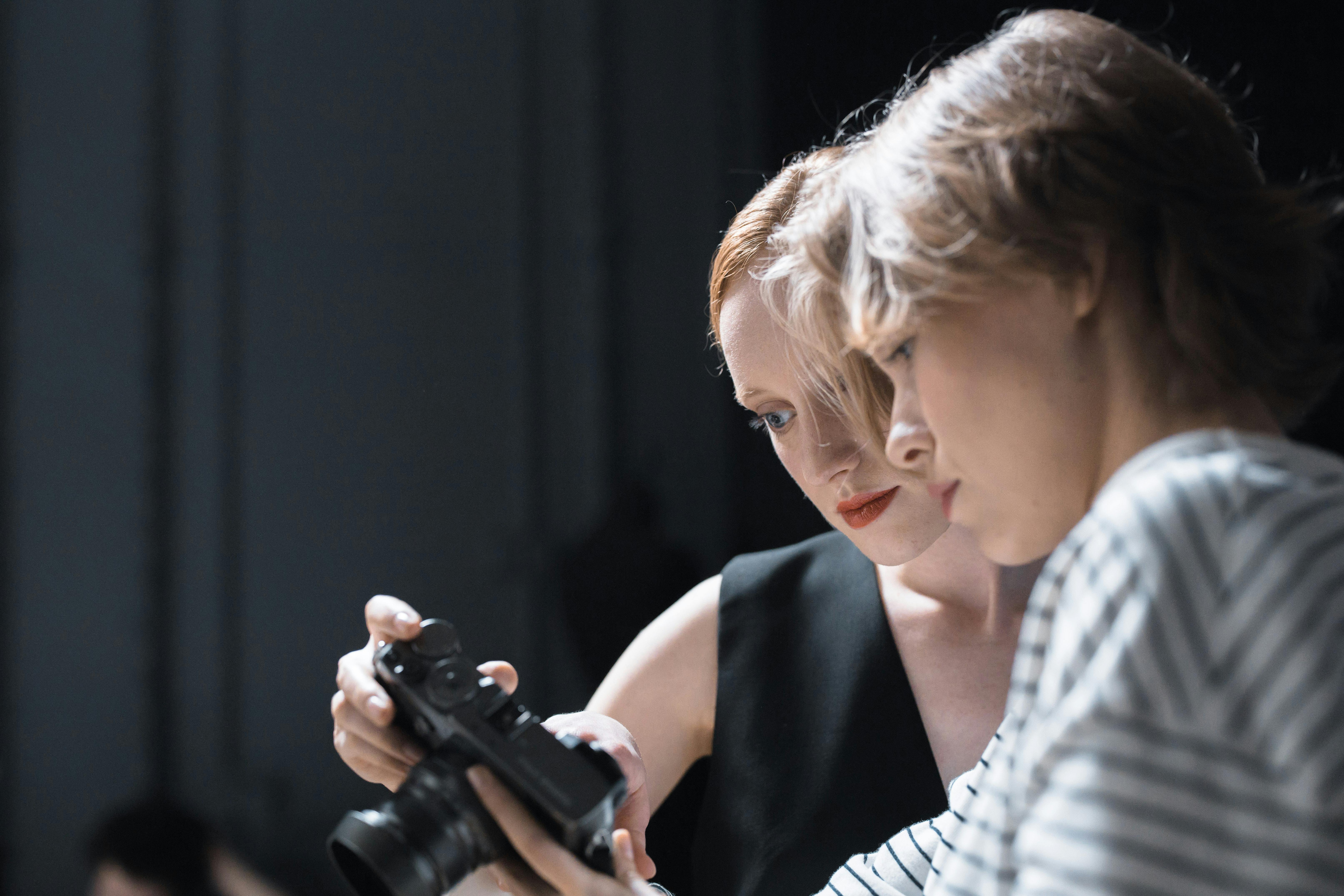 Two women reviewing images on a professional camera indoors.