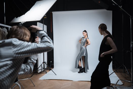 A professional studio shoot featuring a model in a silver dress with a photographer and assistant.