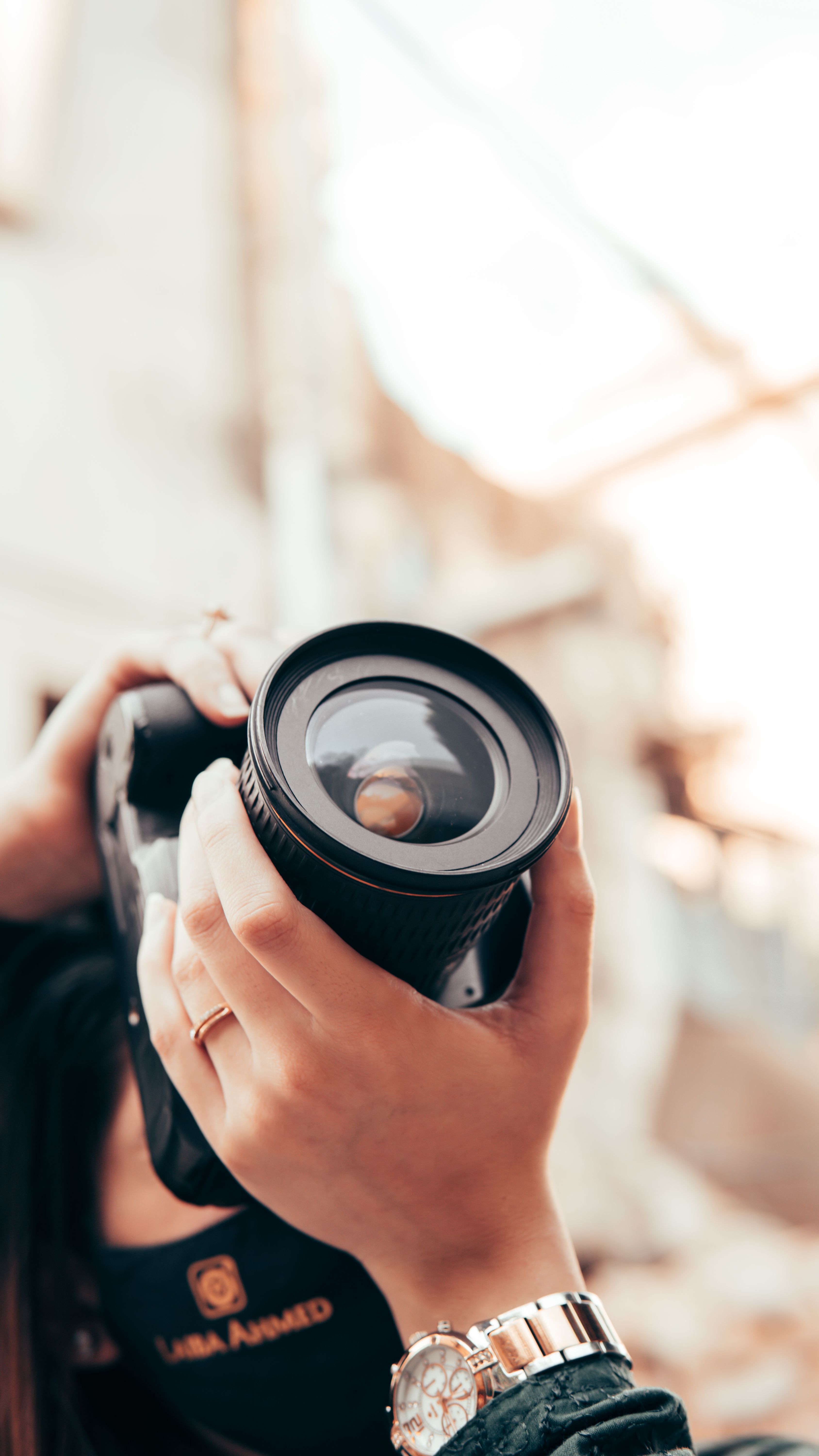 Detailed close-up of hands holding a camera with a lens, taken outdoors.