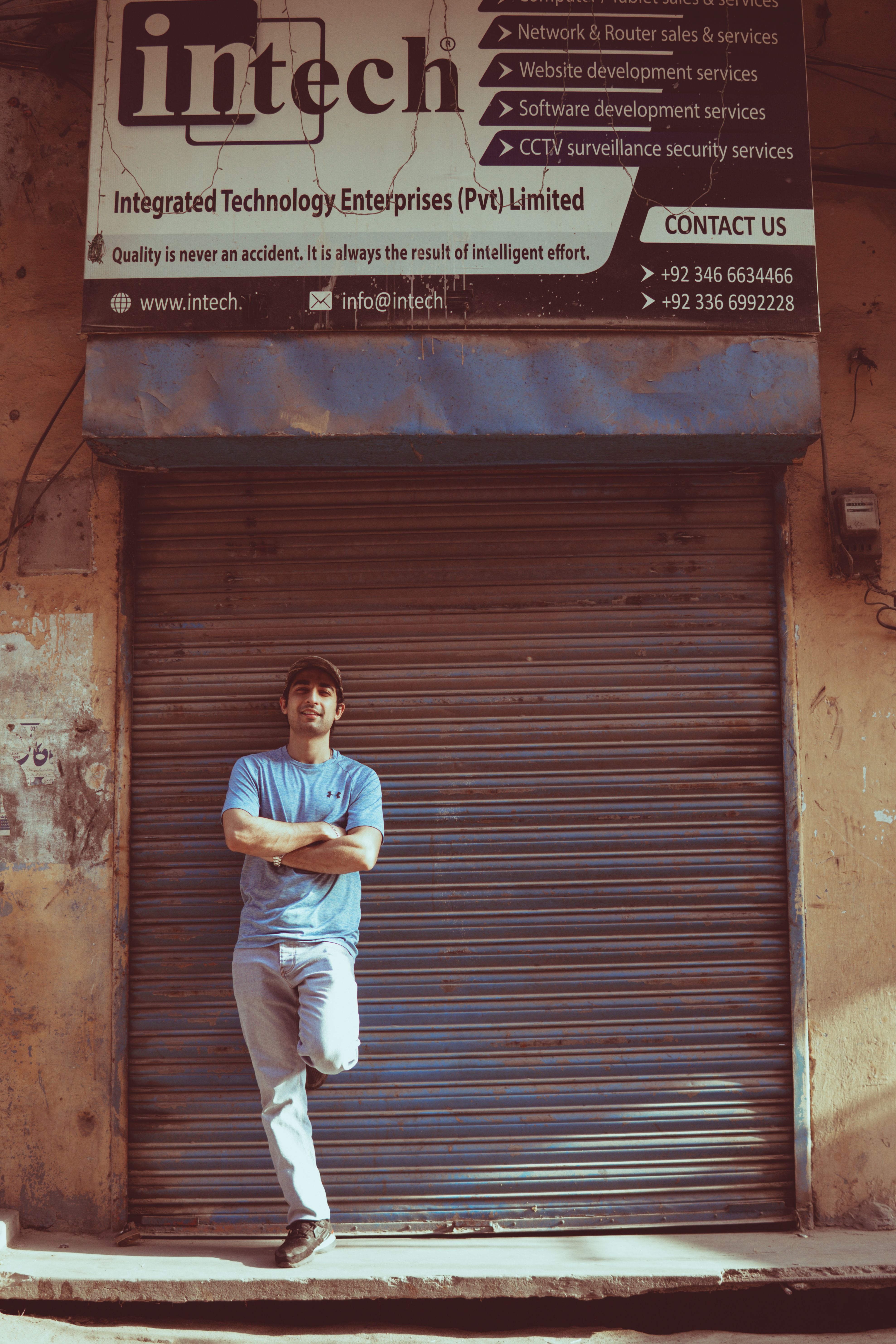 Young man posing confidently in front of a closed shutter in Sialkot, Pakistan.
