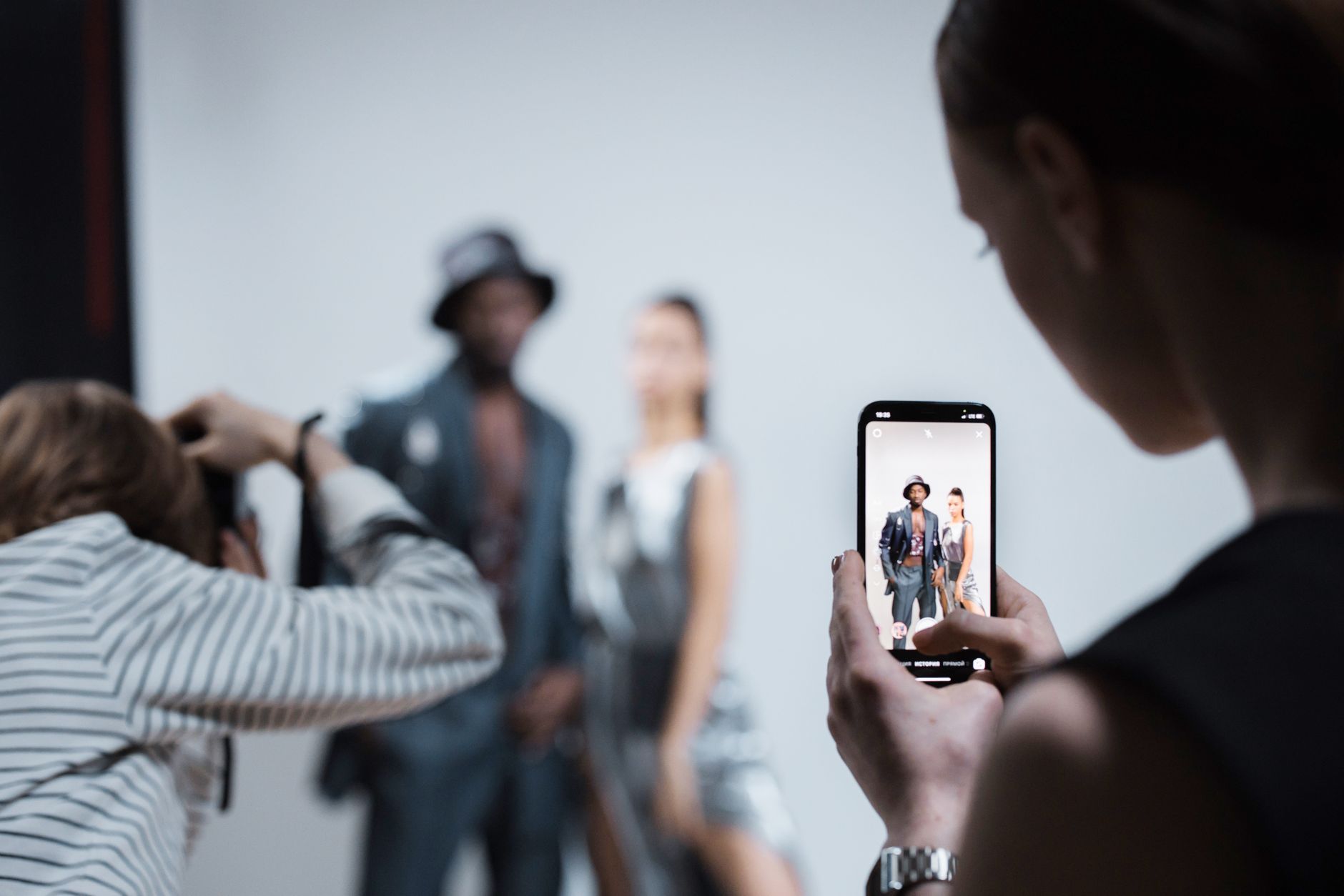 Fashion models being photographed in a professional studio setting with smartphone capture.