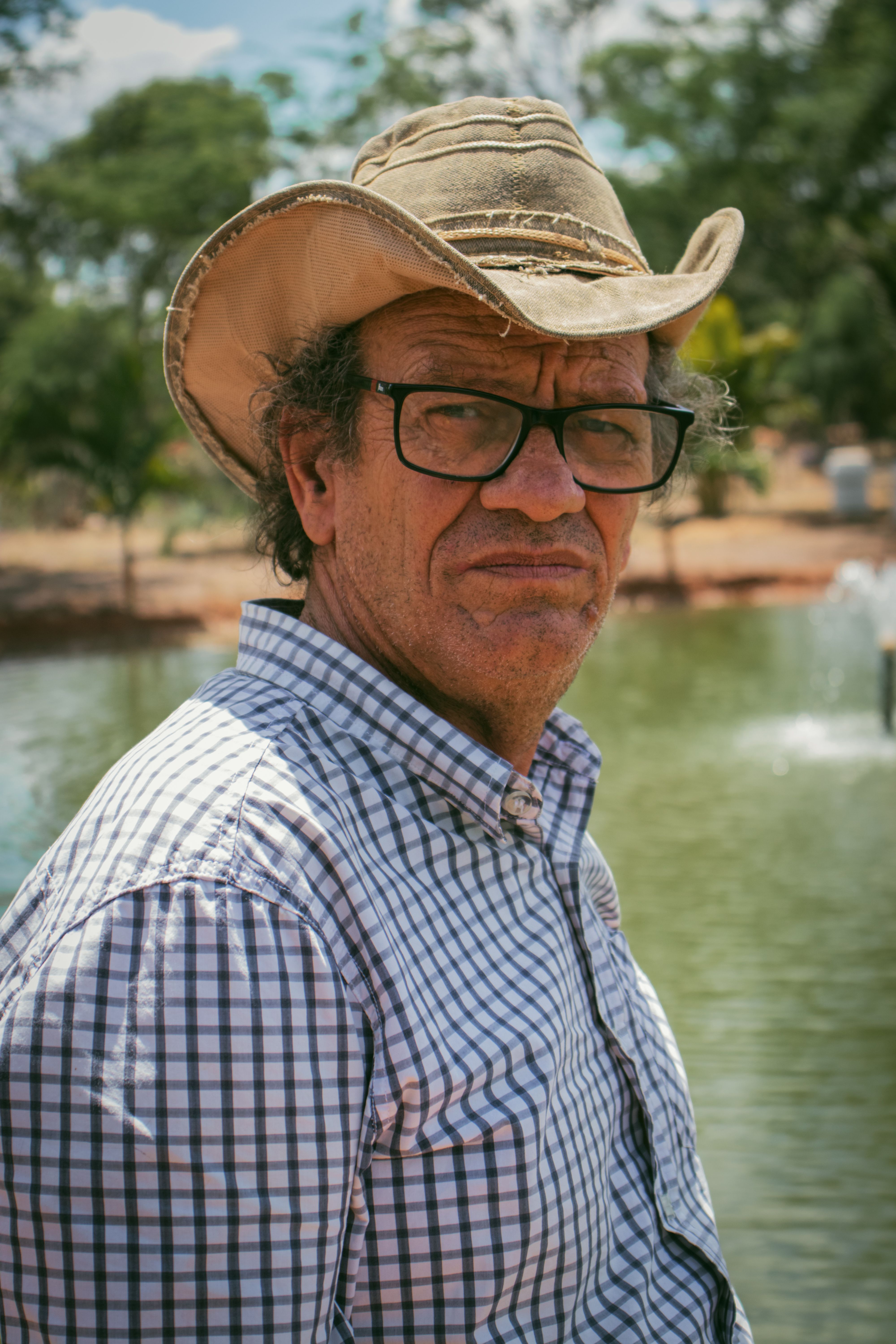 An outdoor portrait of a mature man wearing a hat and glasses by a serene lake.