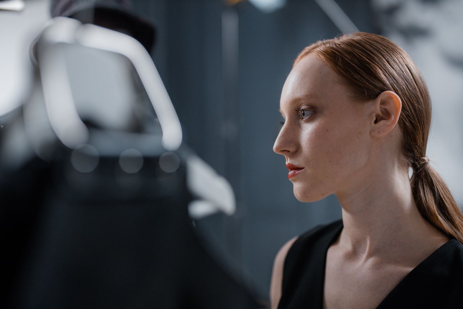 Side profile of a red-haired woman with a low ponytail and black top in soft indoor light