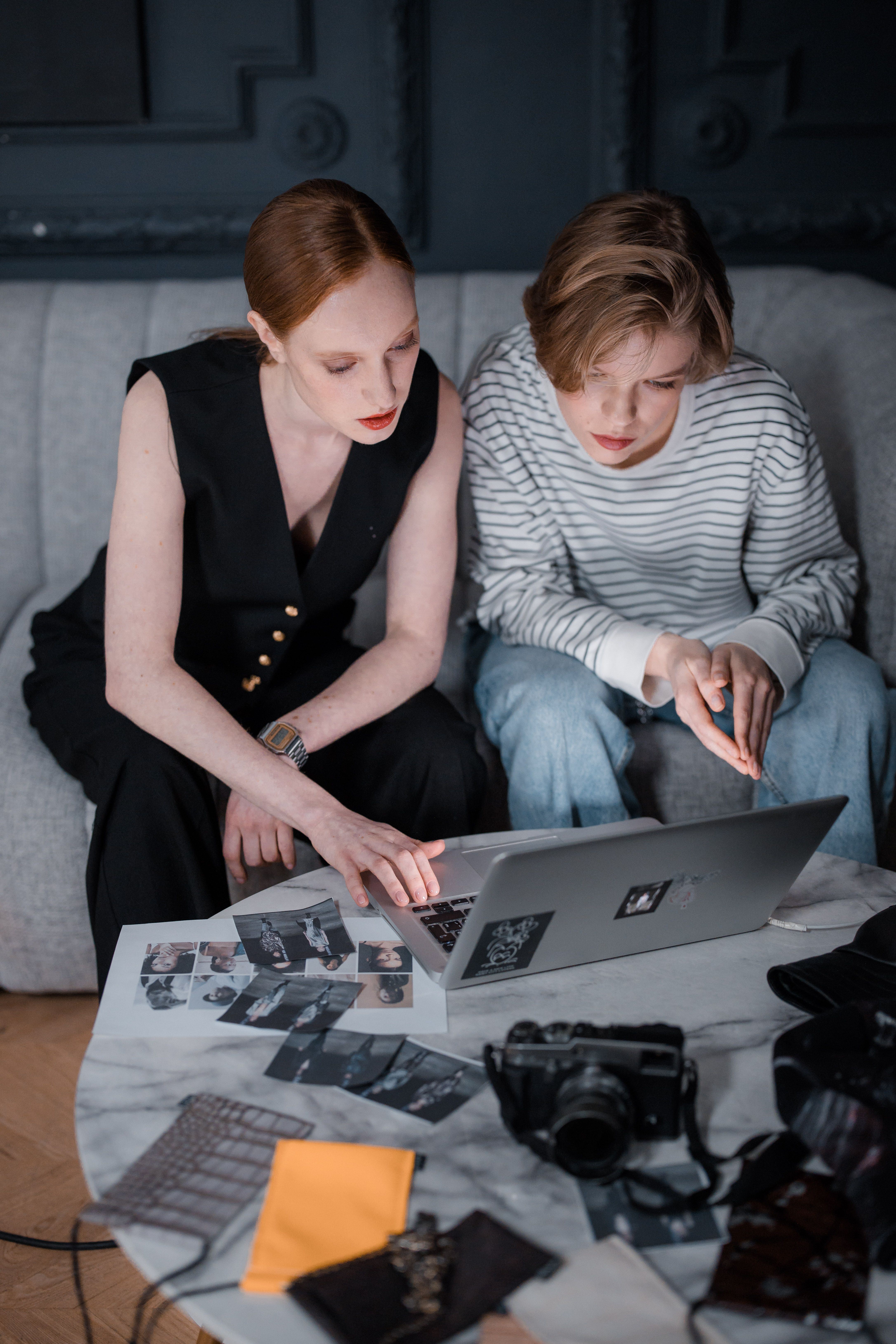 Two people working together on a creative project, reviewing photos on a laptop indoors.