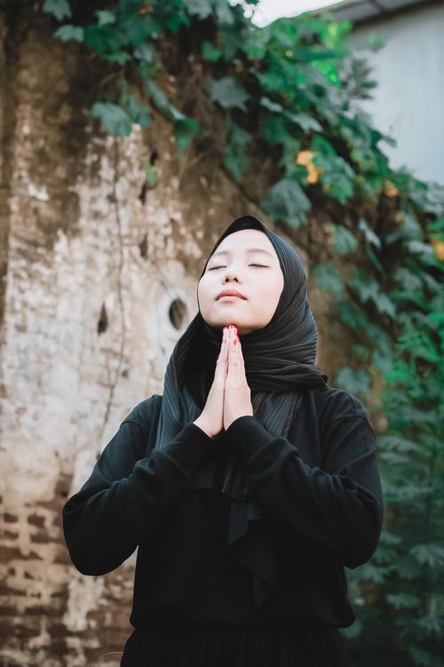 Free Young woman in hijab praying with serenity and focus outdoors surrounded by nature. Stock Photo
