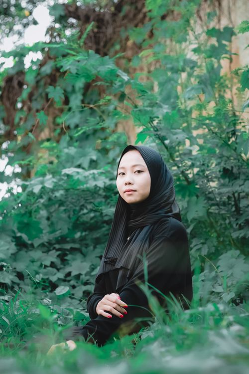 Free A serene portrait of a woman in a hijab amidst vibrant green plants, symbolizing cultural grace. Stock Photo