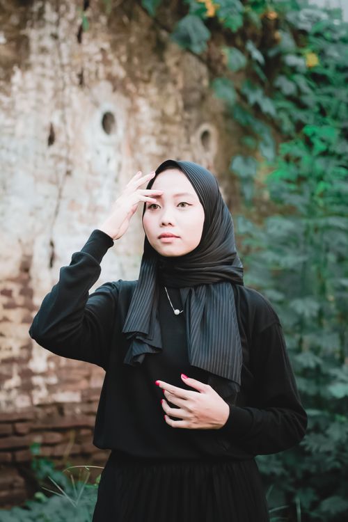 Free Portrait of an Asian woman in a black hijab, outdoors against a rustic wall. Stock Photo