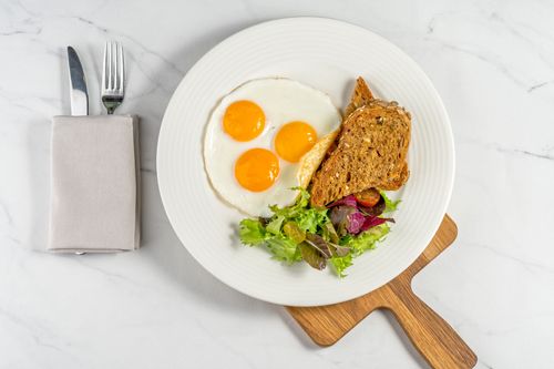 Free A delicious breakfast of sunny side up eggs, toast, and salad served on a white plate. Stock Photo