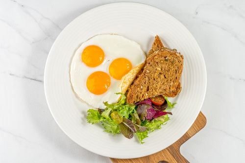 Free Top view of a nutritious breakfast with sunny side up eggs, toast, and salad in Dubai. Stock Photo