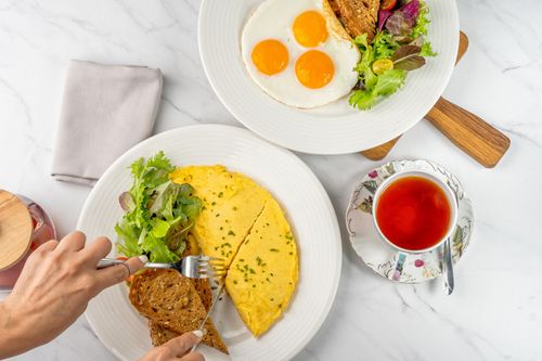 Free Bright breakfast spread featuring omelette, salad, bread, and tea for a fresh start to the day. Stock Photo