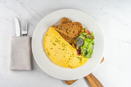 Top-down view of a tasty omelet with salad and toast on a white plate, perfect for breakfast.