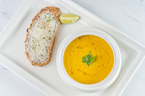 Bowl with Yellow Soup Beside a Bread
