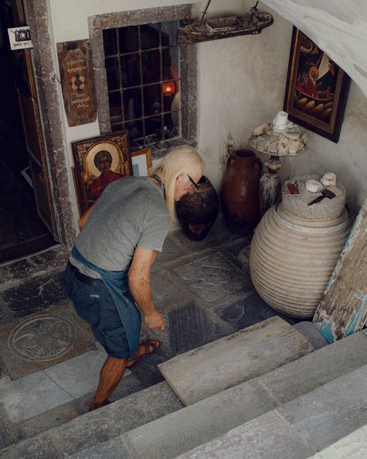 High angle of male worker with long hair in casual clothes and blue apron working near temple entrance with icons on walls