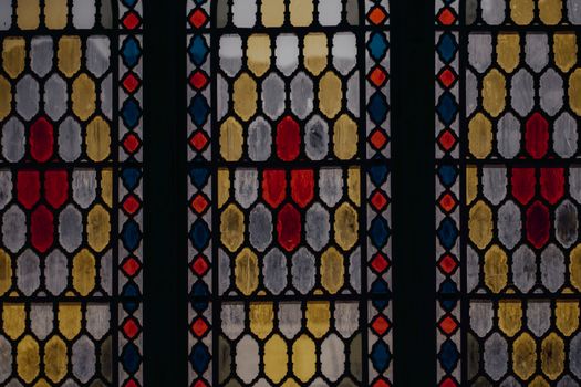 Amazing colorful abstract symmetrical stained glass window with dark wooden frame of building in daylight