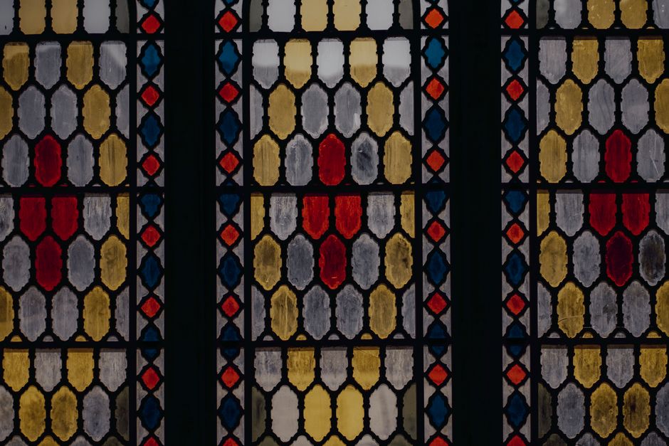 Amazing colorful abstract symmetrical stained glass window with dark wooden frame of building in daylight