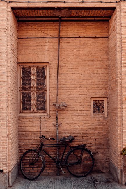 Modern bicycle parked near brick wall of old building under window on pavement on street in daylight