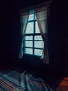 Dark room with window and vintage curtains over bed with colorful blanket on rainy day