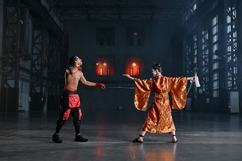 Free Two performers in martial arts costumes engage in a dramatic face-off inside a large industrial hall. Stock Photo