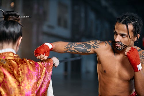 Free A Shirtless Man With Tattoos Punching a Person in Traditional Wear Stock Photo