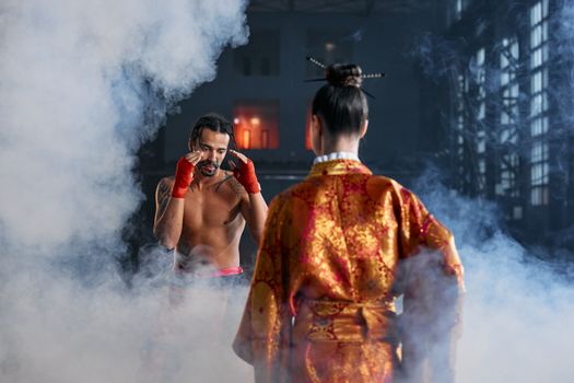 Two martial artists in traditional attire face off in a dramatic, smoke-filled arena.