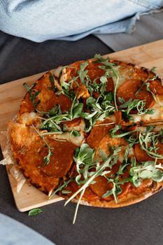 Tasty pepperoni pizza topped with fresh arugula leaves on a wooden cutting board.