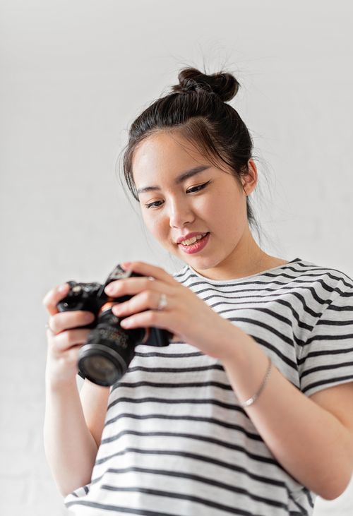 Free Asian woman smiling and examining a camera, wearing a striped shirt. Stock Photo