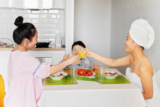 Asian family smiling and toasting at breakfast table in kitchen setting.