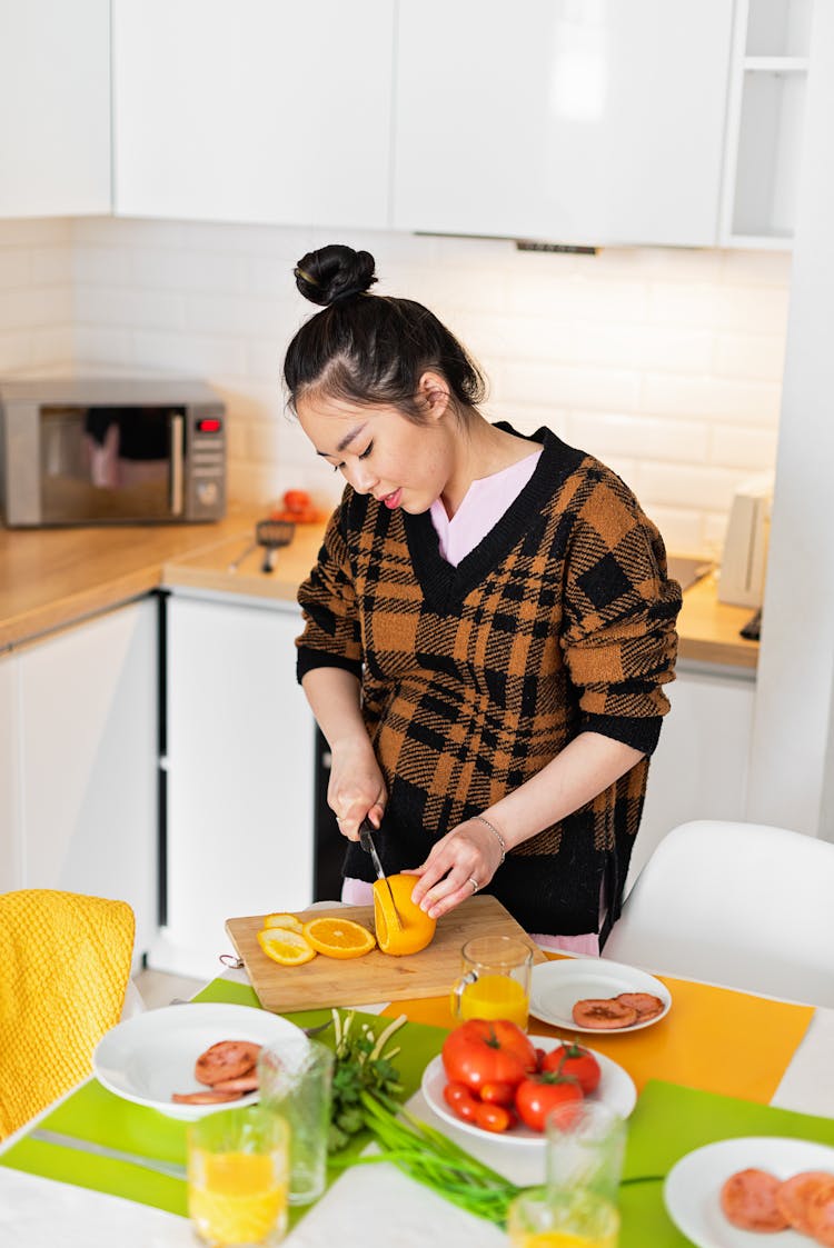 A Woman In Knitted Sweater Slicing An Orange On A Wooden Chopping Board