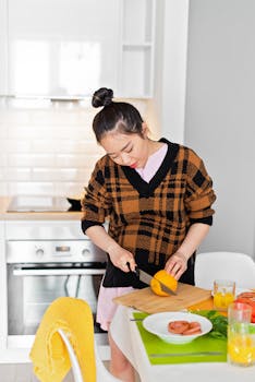 Young woman slicing oranges for fresh juice in an airy kitchen setting. Vibrant colors and natural light enhance the scene.