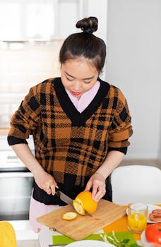 Young woman slicing oranges on a wooden board in a modern kitchen for breakfast preparation.