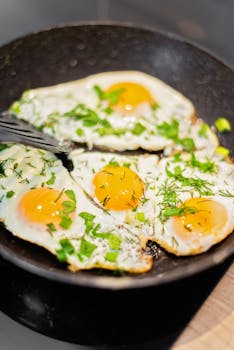 Close-up of fried eggs garnished with herbs, sizzling in a black frying pan. Perfect breakfast inspiration.