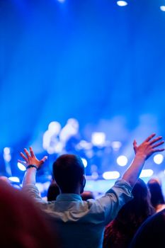 A lively concert scene with audience raising hands, filled with vibrant blue lights.