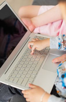 Child's hands typing on a laptop indoors, showcasing learning and technology engagement.