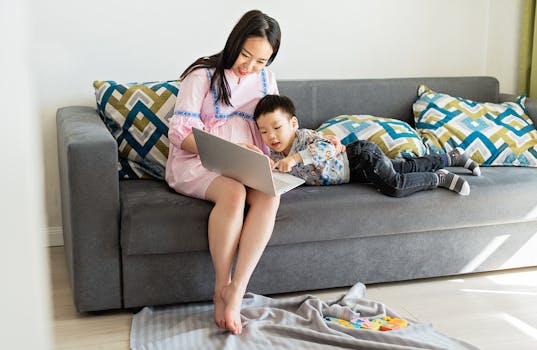 Pregnant mother and son bonding on sofa, using laptop at home.