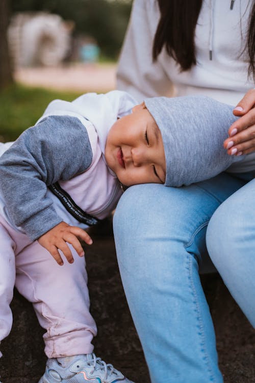 Free Smiling Asian baby in casual clothes and cap cuddling head on knee of mother Stock Photo