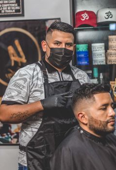 Barber in a mask working attentively on a client's haircut in a contemporary salon setting.