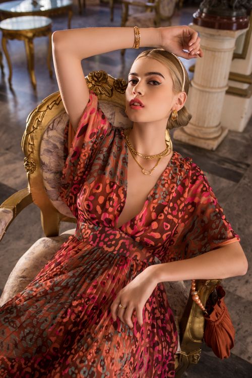 Free Stylish woman posing in a luxurious setting, wearing a vibrant printed dress with gold accessories. Stock Photo