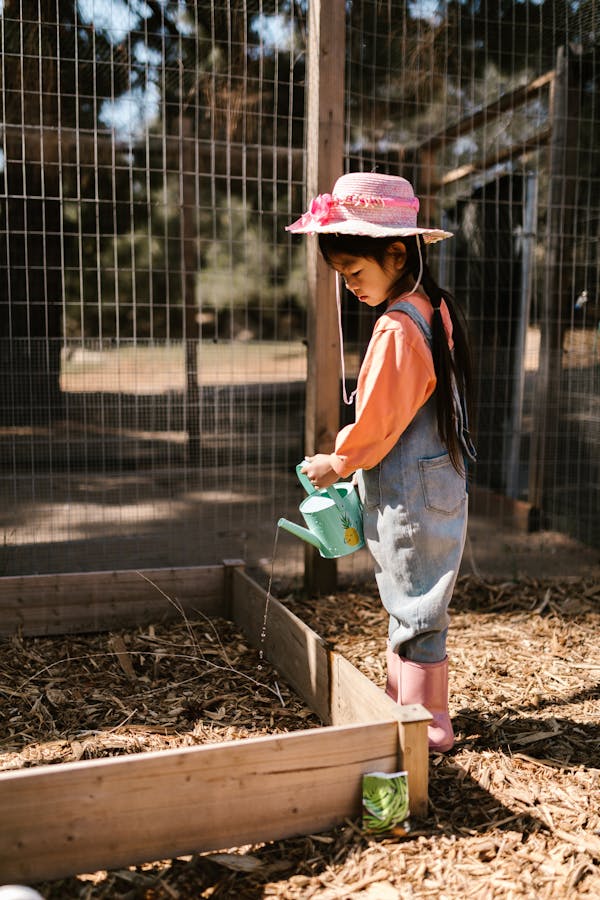 Girl in Overall and Hat Watering Garden