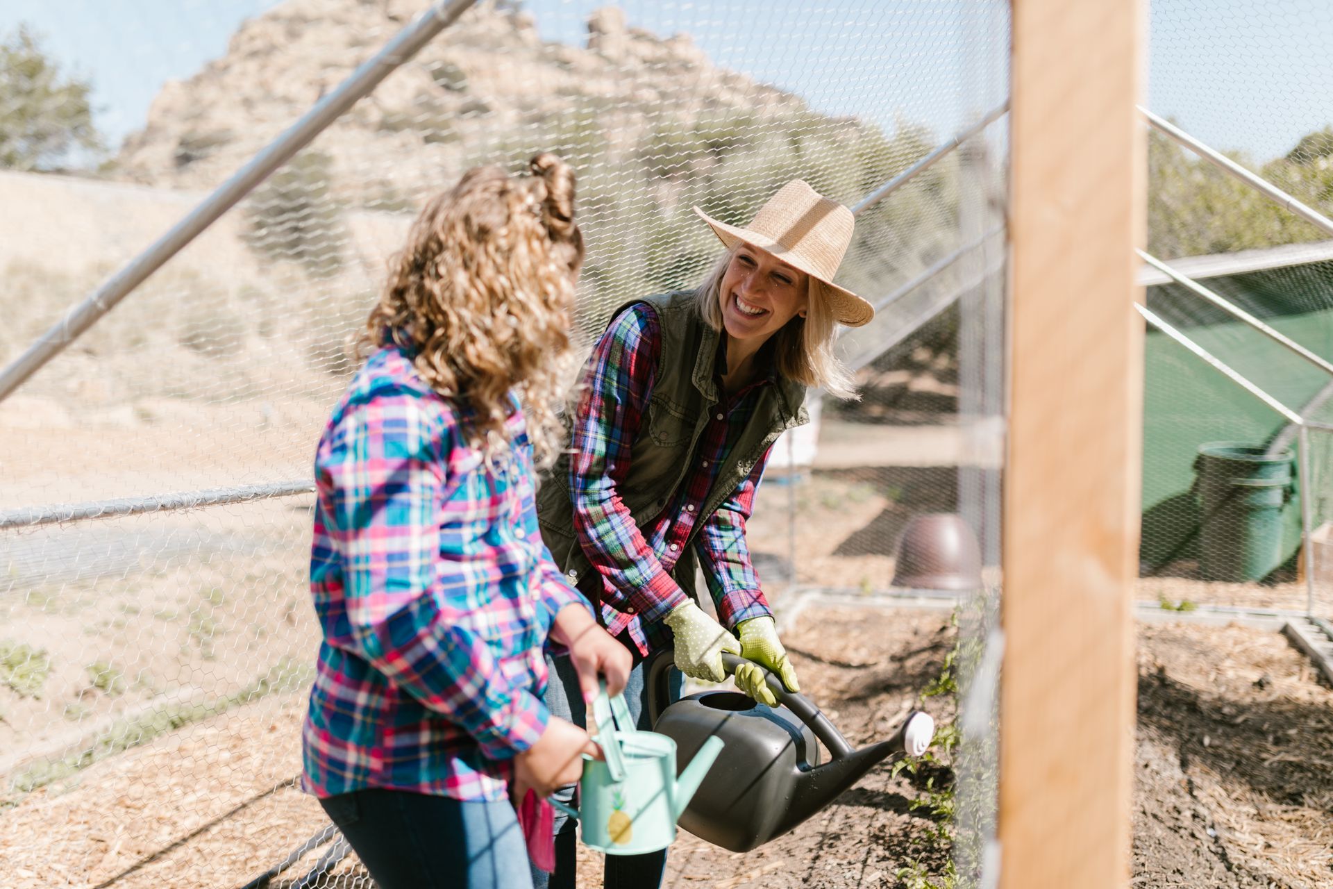 Two Women Wearing Checkered Long Sleeves Watering Plants