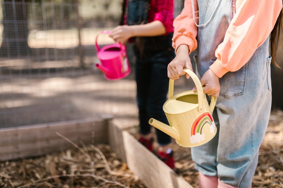 Two children gardening outdoors with colorful watering cans, promoting sustainability.